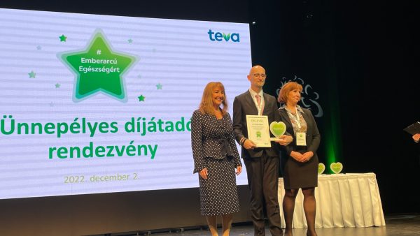Dr. Orbán Zoltán főorvos átveszi a díjat a TEVA cég vezetőitől , akikkel egy nagy a színpadon állnak.