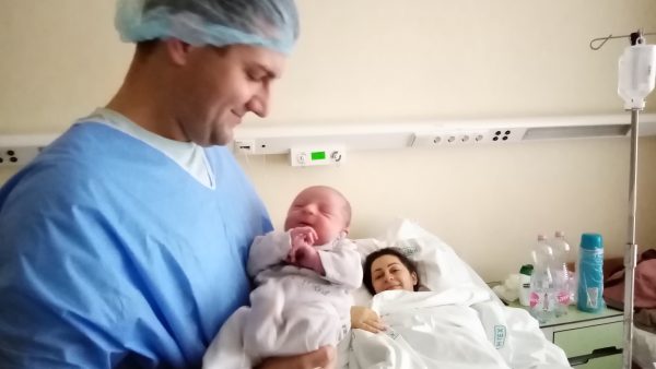 Édesapja karjaiban az újszülött Kornél Márton, háttérben az édesanya pihen a kórház szülészetén található családi szobában