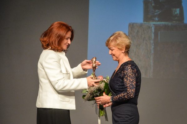 A fotón a díjazott Nagy Éva átveszi az elismerést az alapító Maka Piroskától. A díj egy kisebb méretű bronz szobor, mely egy női alakot ábrázol.