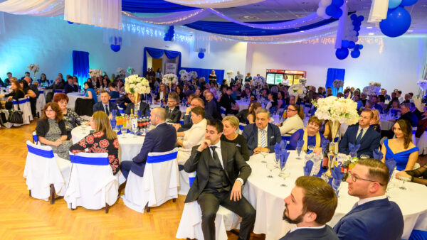 A kép a 2026. február 20-án megrendezett nővérbálon készült, ahol elegánsan öltözött vendégek ülnek kör alakú, fehér abrosszal terített asztaloknál. A terem kék-fehér díszítésben pompázik, a mennyezetről leomló textíliák, fényfüzérek és kék lufik ünnepi hangulatot teremtenek, az asztalokat magas, fehér virágkompozíciók díszítik.