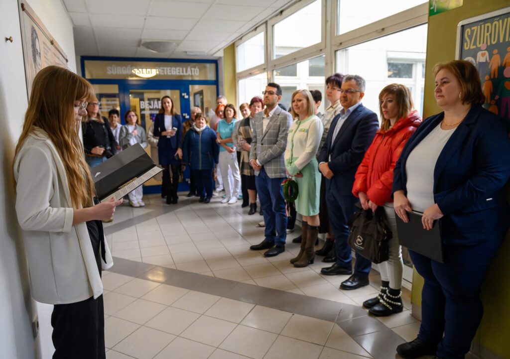 A kép bal oldalán Bognár Diána ápolónő beszédet mond a Kossuth Zsuzsanna emléktábla mellett, a kép jobb oldalán Dr. Kiss Anita főorvos áll, mellette pedig az ünneplő közönség.