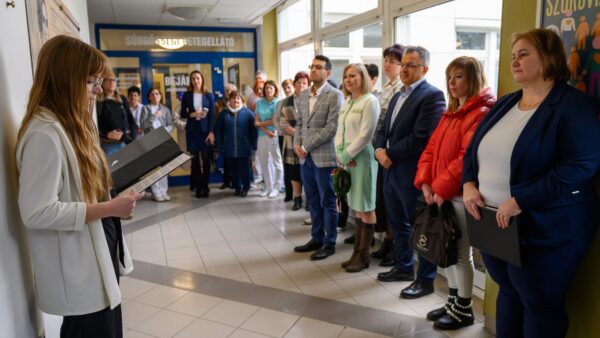 A kép bal oldalán Bognár Diána ápolónő beszédet mond a Kossuth Zsuzsanna emléktábla mellett, a kép jobb oldalán Dr. Kiss Anita főorvos áll, mellette pedig az ünneplő közönség.