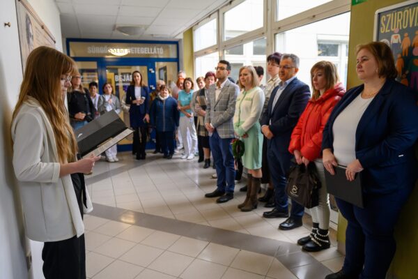 A kép bal oldalán Bognár Diána ápolónő beszédet mond a Kossuth Zsuzsanna emléktábla mellett, a kép jobb oldalán Dr. Kiss Anita főorvos áll, mellette pedig az ünneplő közönség.