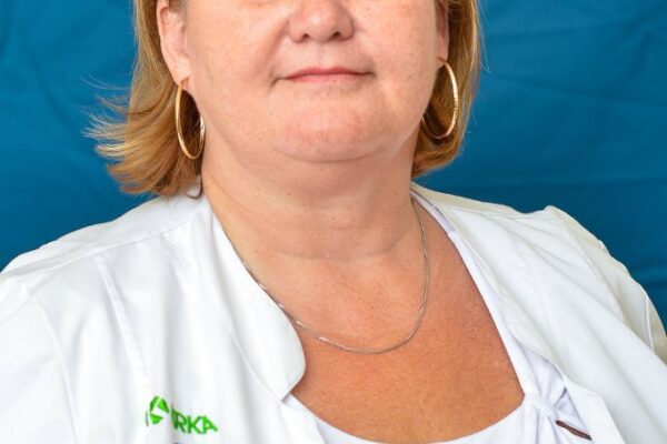 A képen Dr. Kiss Anita, a Gyöngyösi Bugát Pál Kórház újonnan kinevezett orvosigazgató-helyettese látható, vállig érő világosbarna hajjal, világos színű egészségügyi munkaruhában, kék háttér előtt.